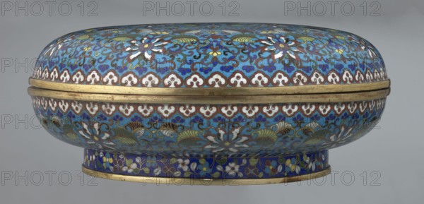 Box with lid, Chinese, Qing dynasty, Qianlong period, cloisonné enamel. Large cylindrical-spheroidal box supported on a separate annular foot, with a slightly flattened lid. Vessel covered by a plant tendril encircling the entire surface container and lid, dominated by chrysanthemum flowers and leaves in various stylistic forms, set against a turquoise background. Upper edge of the storage section and lower edge of the cover decorated with a border of ruyi-heads in white and red; a blue three-petal pattern completes the decoration. Foot decorated with an ornamental band of colorful flowers and leafy twigs. Interior of the box and inner surface of the foot filled with uniform turquoise enamel. Unenamelled edges of the storage section, cover, and foot are gilded. 18th century, China. Height 14.5 cm; diameter 34.5 cm., A rounded, lidded decorative container with a low pedestal base is shown, covered all over in intricate floral and foliate enamel patterns. The dominant color is turquoise ...