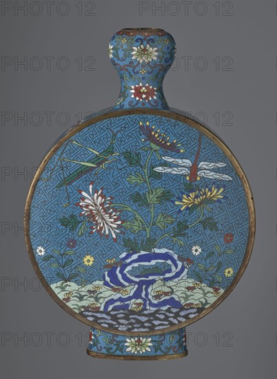 Vase - moon bottle pilgrim bottle with a flattened belly, supported by a separate oval high foot, with a short neck resembling a garlic bulb suantoukou type. Decoration on one side: a multicolored composition depicting a chrysanthemum flower growing on a coastal rock, above which a dragonfly and a grasshopper hover. The other side shows lilies irises on a rock above the water, with a butterfly and a grasshopper above them. Small, colorful shore flowers appear in both representations. Both compositions use the flowers and birds motif known from Chinese scroll painting. A Chinese meander forms the background for both compositions. The foot, side edges, and neck are filled with a lotus tendril. Colors dominated by red, white, green, yellow, and navy blue. Elements without enamel decoration are gilded; there are visible abrasions of the gilding and firing-related technological defects. Cloisonné enamel. Qing dynasty 2nd half 18th century. China. Vessel. Height 29.8 cm, width 21.1 cm., A ro...