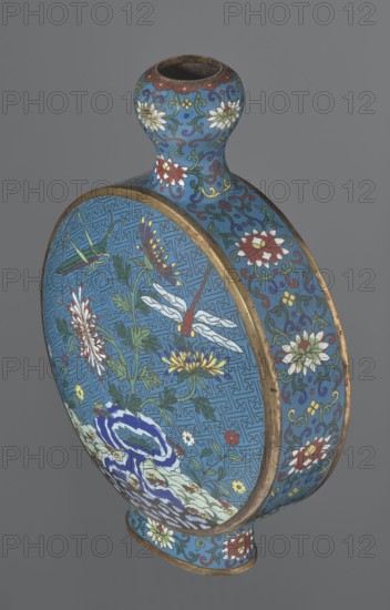 Vase - moon bottle pilgrim bottle with a flattened belly, supported by a separate oval high foot, with a short neck resembling a garlic bulb suantoukou type. Decoration: On one side a multicolored composition depicting a chrysanthemum growing on a coastal rock, above which a dragonfly and a grasshopper hover. The other side shows lilies irises on a rock above the water, with a butterfly and a grasshopper above them. Small colorful flowers growing on the shore appear in both compositions. Motifs derive from the Chinese flowers and birds scroll-painting tradition. A Chinese meander forms the background for both compositions. Foot, side edges, and neck are filled with a lotus tendril. Colors dominated by red, white, green, yellow, and navy blue; elements without enamel are gilded. Visible abrasions of the gilding and technological firing defects. Cloisonné enamel. Qing dynasty, 2nd half 18th century. China. Vessel. Height 29.8 cm; width 21.1 cm., A rounded, flattened vase with a narrow ne...