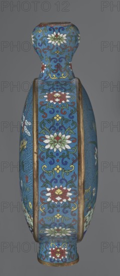 Vase - moon bottle pilgrim bottle with a flattened belly, supported by a separate oval high foot, with a short neck resembling a garlic bulb suantoukou type. Decoration on one side: a multicolored composition depicting a chrysanthemum flower growing on a coastal rock, above which a dragonfly and a grasshopper hover. The other side shows lilies irises on a rock above the water, with a butterfly and a grasshopper above them. Small colorful flowers growing on the shore appear in both representations. Both compositions use the flowers and birds motif known from Chinese scroll painting. A Chinese meander forms the background for both compositions. The foot, side edges, and neck are filled with a lotus tendril pattern. Colors dominated by red, white, green, yellow, and navy blue; elements without enamel decoration are gilded. Visible abrasions of the gilding and technological firing defects. Cloisonné enamel. Qing dynasty Qing style, 2nd half 18th century, China. Height 29.8 cm, width 21.1 c...