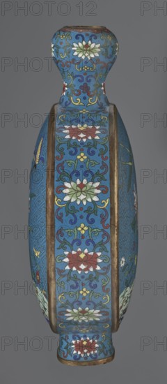 Vase - moon bottle pilgrim bottle with a flattened belly, supported by a separate oval high foot, with a short neck resembling a garlic bulb suantoukou type. Decoration on one side: multicolored composition depicting a chrysanthemum growing on a coastal rock, above which a dragonfly and a grasshopper hover. Other side: composition showing lilies irises on a rock above the water, with a butterfly and a grasshopper; small colorful flowers growing on the shore visible in both representations. Motif derives from Chinese flowers and birds scroll painting. A Chinese meander forms the background for both compositions. Foot, side edges, and neck filled with a lotus tendril; palette dominated by red, white, green, yellow, and navy blue. Elements without enamel are gilded; visible abrasions of the gilding and firing-related technological defects. Cloisonné enamel. Qing dynasty 1644–1911, 2nd half 18th century. Chinese. Vessel. Height 29.8 cm; width 21.1 cm., A tall vase with a rounded shoulder a...