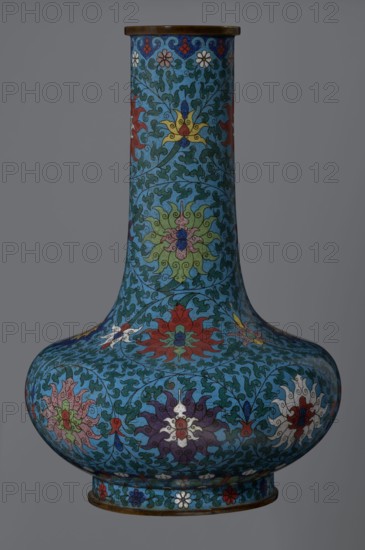 Vase, noted. Chinese, Qing dynasty 2nd half of the 18th century. Cloisonné enamel vase with long, wide neck on a separate ring-shaped foot, flattened spherical belly decorated overall with a dense, multicolored lotus tendril motif. Foot has an ornamental band of small flowers and leaves. Upper neck rim features a border of ruyi-heads; neck ends with a thick ungilded metal ring. Height 37.8 cm; diameter 15.5 cm., A tall, bulbous vase with a narrow neck and flared rim, covered in intricate floral and vine patterns in a dominant blue background with teal leafy motifs; the surface features several stylized flowers in colors including red, yellow, green, purple, white, and pink, arranged in repeating medallion-like forms; the rim and base have a thin metallic brown band, and a ring of small floral motifs in various colors encircles the base; the overall palette is dominated by shades of blue and teal with accents of red, yellow, green, purple, white, pink, and brown.