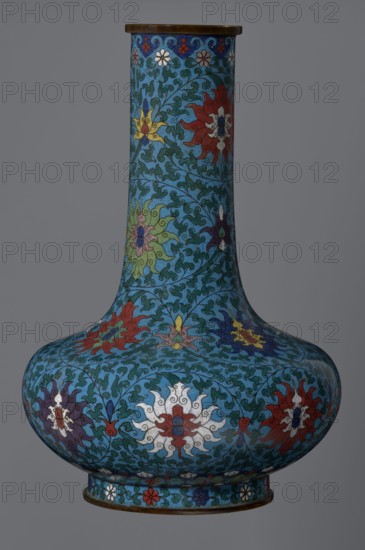 Vase, gift; Chinese, Qing dynasty 1644–1911, cloisonné enamel; 2nd half of the 18th century. Vase with a long, wide neck, supported on a separate ring-shaped foot, with a flattened spherical belly; main decoration is a dense, multicolored lotus tendril surrounding the entire surface. Foot decorated with an ornamental band of small flowers and leaves. Upper edge of the neck at the rim decorated with a border formed of ruyi-heads. Neck ends with a thick, ungilded metal ring. Height 37.8 cm; diameter 15.5 cm., A tall, bulbous vase with a narrow neck decorated in a dense scrolling vine pattern on a blue background, featuring stylized floral motifs in red, white, yellow, green, purple, and dark blue, with a band of small floral medallions near the base and a thin metallic rim at the top and bottom; the surface shows intricate curving leaves and petals in contrasting shades of green and teal against the dominant blue field.