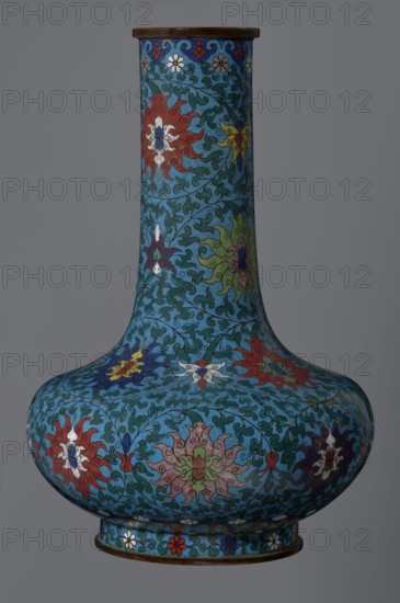 Vase, gift, Chinese, Qing dynasty 1644–1911, cloisonné enamel; subject: lotuses and lotus tendrils as ornament. Vase with a long, wide neck supported on a separate ring-shaped foot, flattened spherical belly densely decorated with multi-colored lotus tendrils surrounding the entire surface. Foot decorated with an ornamental band of small flowers and leaves. Upper edge of the neck at the rim decorated with a border of ruyi-heads. Neck ends with a thick, ungilded metal ring. 2nd half of the 18th century, China. Vessel; height 37.8 cm, diameter 15.5 cm., A tall, bulbous vase with a narrow neck and flared lip decorated all over with intricate floral and foliate patterns in shades of blue, turquoise, green, red, white, yellow, purple, and brown; the background is predominantly teal-blue with swirling dark green vine motifs, and the floral rosettes appear in red, white, yellow, purple, pink, and green with darker outlines; the rim and base edges are brown, and a few small flower motifs in wh...