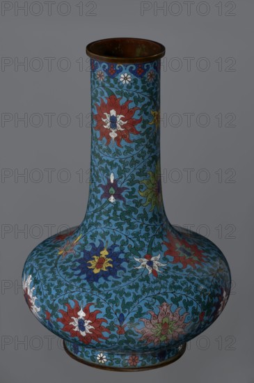 Vase, noted; Chinese, Qing dynasty 2nd half of the 18th century; cloisonné enamel. Vase with a long, wide neck supported on a separate ring-shaped foot, with a flattened spherical belly; main decoration is a dense, multicolored lotus tendril surrounding the entire surface. Foot decorated with an ornamental band of small flowers and leaves. Upper edge of the neck at the rim is decorated with a border formed of ruyi-heads. Neck ends with a thick, ungilded metal ring. Vessel; height 37.8 cm, diameter 15.5 cm., A tall vase with a narrow cylindrical neck and a wide rounded base, decorated all over with swirling floral motifs and leafy tendrils in a palette of blue, turquoise, red, white, yellow, green, purple, and brown, with a darker brown rim and base edge; the background is primarily blue and turquoise while stylized flowers in red, white, yellow, purple, and green repeat across the surface, and fine dark outlines define the scrolling leaf patterns.