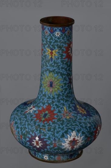 Vase, Chinese, Qing dynasty 2nd half of the 18th century. Cloisonné enamel vessel with a long, wide neck supported on a separate ring-shaped foot and a flattened spherical belly. Main decoration: dense, multi-colored lotus tendril surrounding the entire surface. Foot decorated with an ornamental band of small flowers and leaves. Upper edge of the neck at the rim has a border formed of ruyi-heads. Neck ends with a thick, ungilded metal ring. Height 37.8 cm; diameter 15.5 cm., A tall, bulbous vase with a long narrow neck decorated with an intricate floral pattern in shades of blue, turquoise, red, green, yellow, white, purple, and pink, with scrolling vine-like motifs and stylized flower forms covering the entire surface, a dark brown rim at the top and a darker base at the bottom, photographed against a plain gray background.
