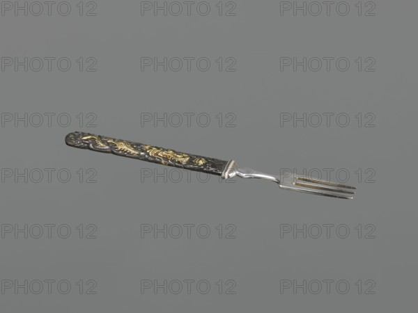 Fork with knife handle kozuka, Japanese; Edo period 1603–1868, 18th century; materials/objects: fork with kozuka-style knife handle, cutlery; motifs: dragons and fish; function: melee weapon/kozuka for katana; dimensions: height 16.8 cm, width 1.4 cm., A single fork is shown against a gray background, with a metallic silver pronged end and a long decorative handle that appears dark, almost black, with raised ornate patterns highlighted in gold; the handle has textured carved details and a slightly rounded end, and the metal shaft connecting the handle to the prongs is shiny silver with subtle reflections.