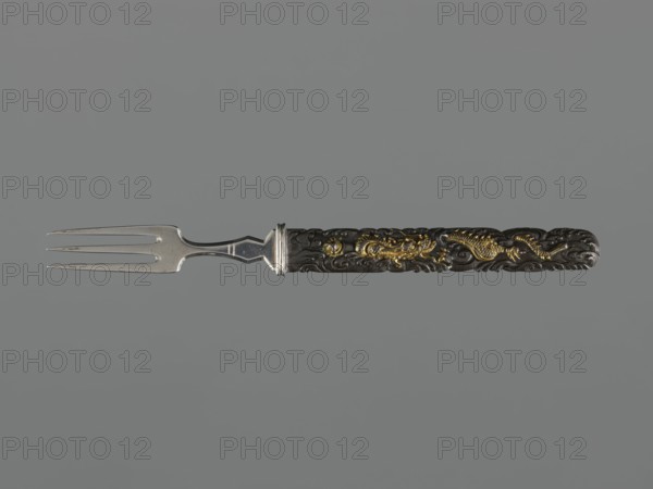 Fork with knife handle kozuka, Japanese, Edo period 18th century, 1603–1868, kozuka for sword, decorated with dragons and fish, materials: metal cutlery, height 16.8 cm, width 1.4 cm., A metal two-pronged fork with a silver-toned tined end and a dark ornate handle featuring raised decorative patterns and gold-colored embellishments, shown horizontally against a plain gray background.