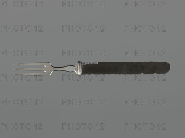 Fork with knife handle kozuka, Japanese, Edo period 1603–1868, 18th century; materials: metal cutlery; subject/iconography: dragons and fish; function: kozuka knife handle for a katana; dimensions: height 16.8 cm, width 1.4 cm; melee weapon accessory., A metal fork with three tines and a silver-colored neck is shown horizontally against a neutral gray background, the handle extending to the right and appearing dark brown to nearly black with a textured, scalloped edge. The fork's metal portion has a reflective silver tone with some darker spots and slight surface wear, while the handle is matte and richly dark, creating contrast with the silver. The overall composition is centered and minimal, featuring the contrasting silver and dark brown or black colors on a gray backdrop.