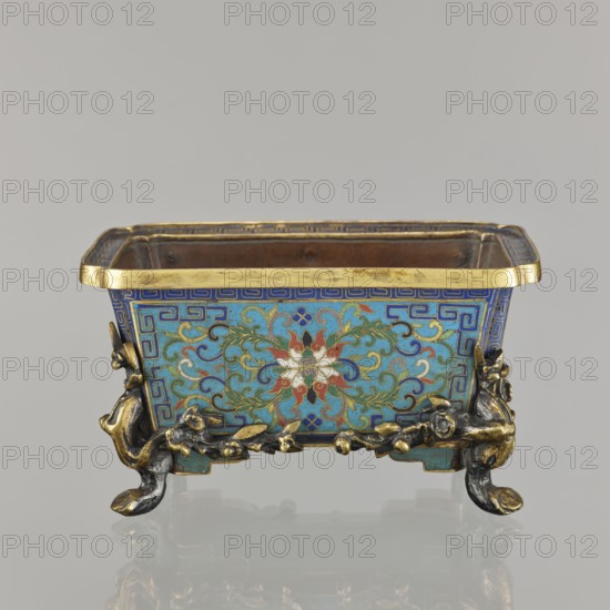 Flower pot incense burner on four legs, Chinese, Qing dynasty 1644–1911, cloisonné enamel, 18th century. Decoration: lotus tendril on a turquoise background; legs shaped as flowered trunks plum branches in gilded bronze. Motifs: lotuses, plum trees, cracked ice, meander. Function: jardiniere/incense burner. Dimensions: height 9.5 cm; width 17.2 cm; depth 12.0 cm., A rectangular decorative vessel sits on a reflective surface, showing a palette of blue, turquoise, gold, red, white, green, and black. The vessel has a gold rim and ornate patterned sides with swirling floral motifs in turquoise, blue, green, red, and white set against a blue background with a geometric border. The base features sculpted metallic feet and decorative elements in gold and dark metal tones, with organic vine-like forms and rounded protrusions. The interior appears darker, with a metallic brownish surface. The overall shape is rectangular with slightly flared top edges and a symmetrical decorative scheme on the ...