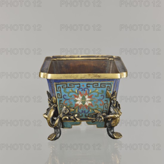 Flower pot incense burner on four legs, 18th century, China, Qing 1644–1911. Cloisonné enamel vessel, jardinière/incense burner; decoration: lotus tendril on a turquoise background, legs shaped as flowered trunks plum branches made of gilded bronze; motifs include lotuses, lotus tendril, plum trees, cracked ice, and meander ornament. Dimensions: height 9.5 cm, width 17.2 cm, depth 12.0 cm., A small square metal container with a flared gold rim sits against a plain light gray background; its exterior surfaces are decorated with a turquoise blue base and intricate patterns in darker blue, green, red, white, and gold forming a stylized floral motif on the visible side. The container rests on ornate feet shaped like twisted branches and animal-like forms in dark metal with gold highlights. The interior appears brown and worn, while the exterior corners show geometric border patterns in blue and gold. The overall colors visible include turquoise blue, dark blue, green, red, white, gold, dar...