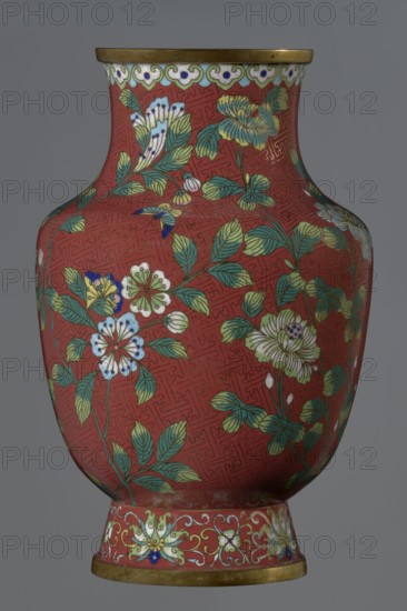 Vase, ; Chinese; Qing dynasty Xianfeng, 1851–1861; cloisonné enamel; subject: flowers, floral pattern, plum branches and meander ornament; description: set on a tall conical foot flaring downwards and terminating in a metal ring, foot decorated with a lotus tendril; short wide neck topped with a metal ring, below which is a border of ruyi-heads; belly and neck decorated with an all-around composition of flowers and plum branches against a red Chinese meander background; date: 1st half of the 19th century; origin: China; vessel; height 25.1 cm, diameter 16.5 cm, weight 1.5 kg., A rounded vase with a flared neck and foot, predominantly red in color, decorated with a pattern of green leaves and stems and flowers in shades of white, pale yellow, blue, and green, with touches of dark blue and gold outlining and accents; the rim and base edges have a metallic gold band, and the foot features a decorative border with scrolling motifs in light green, blue, and white against the red ground; the...