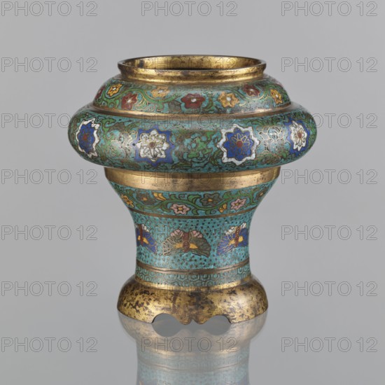 Vessel, Meiji period late 19th century, 1868–1912, Japan. Champlevé enamel decoration with plant motifs, butterflies, flowers, and fans; sasarindo coat of arms. Height 28 cm; diameter 28.6 cm., A short, rounded metal vessel with a flared rim and a bulbous upper section sits against a plain neutral background; its surface is decorated with intricate enamel patterns in turquoise, blue, green, white, red, yellow, and gold, including floral motifs and stylized shapes arranged in bands around the body; the rim and two horizontal bands are gilded with worn gold tone, and the lower base shows a mottled gold appearance with areas of darker patina; the piece casts a subtle reflection on the surface beneath it.