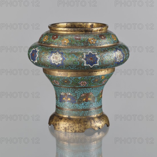 Vessel, gift, Meiji period 1868–1912, Japan; champlevé enamel; plant motifs, butterflies, flowers, fans; sasarindo coat of arms; 19th century; height 28 cm, diameter 28.6 cm., An ornate metal vessel with a rounded bulbous rim narrowing into a flared base sits against a plain light gray background; the vessel displays a dominant turquoise enamel with decorative bands of green, blue, white, pink, yellow, red, and gold; floral and star-like motifs in blue, white, yellow, and pink appear within scrolling green patterns on the upper bulge, while small flower motifs and fan-shaped designs in blue, gold, red, and brown decorate the lower neck; the rim, narrow central band, and scalloped foot show worn gold tones with areas of darker patina, and the vessel casts a soft reflection on the surface beneath it.