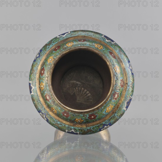 Vessel, Meiji period 1868–1912, Japan. 19th century. Champlevé enamel decoration with plant motifs, butterflies, flowers, and fans; sasarindo coat of arms. Height 28 cm; diameter 28.6 cm., A round ornate vessel rim viewed from above showing an open dark interior with faint engraved fan shapes at the bottom, surrounded by a wide decorative band featuring a repeating floral and scroll pattern in turquoise green, blue, red, yellow, white, and gold, with a visible reflective surface beneath that mirrors parts of the vessel; the background is a uniform light gray.