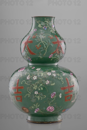Vase, calabash form, 18th century, Qing dynasty, China. Porcelain/ceramic vessel, height 34.3 cm, diameter 24.0 cm. Decoration on a green background with flowers, butterflies, fruit peaches, lingzhi, peonies and floral ornament; pictographic signs among the plant motifs. Chinese art; Qing style., A double-gourd porcelain vase with a glossy green ground decorated with floral vines, blossoms, and berries in colors including pink, red, purple, blue, and gold, and featuring several bold red graphic shapes on both bulbous sections; the vase has a narrow neck, a flared rim with a thin brown edge, and a green foot with a thin brown band at the base, all set against a neutral gray background.