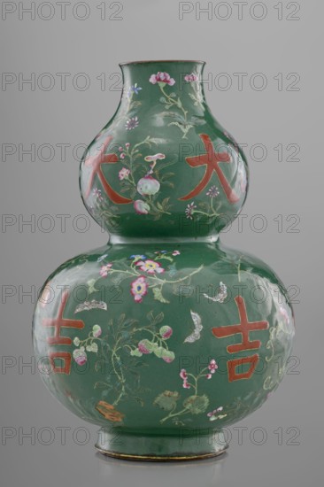 Vase, calabash form, 18th century China, Qing dynasty. Porcelain vessel with decoration on a green background featuring flowers, butterflies, fruit peaches, lingzhi, peonies, and pictographic signs among the plant motifs. Height 34.3 cm; diameter 24.0 cm. Chinese art; floral ornament; Qing style., A double-gourd shaped ceramic vase with a glossy deep green surface decorated with painted floral and botanical motifs in pink, light green, pale blue, white, and gold tones, along with several large reddish-orange symbol-like marks; the vase has a narrow neck, a rounded midsection, and a flared foot with a thin gold rim, photographed against a neutral gray background.