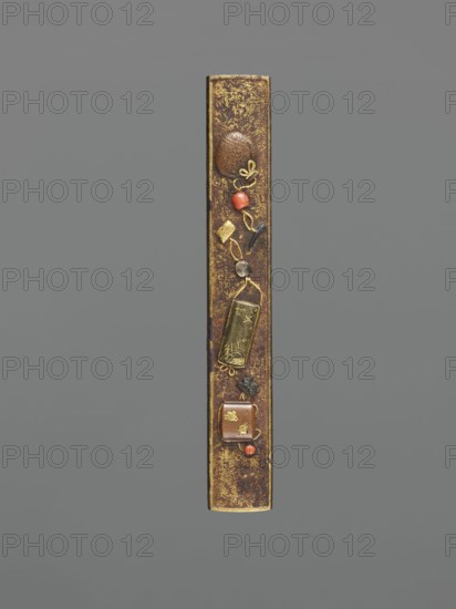 Knife handle kozuka, Japanese, Edo–Meiji period 19th century, Edo/Meiji, 1603–1912, weapons/edged weapons for katana, inrô, netsuke context, height 9.8 cm, width 1.5 cm, A narrow vertical object with a mottled brown surface and gold accents is centered against a plain gray background; along its length are a few small decorative elements including a round textured brown piece, a couple of smooth red-orange beads, small gold-colored shapes and filigree, a rectangular gold-toned plate with an etched pattern, a small dark irregular piece, and a square brown element with gold accents, all arranged in a vertical sequence.
