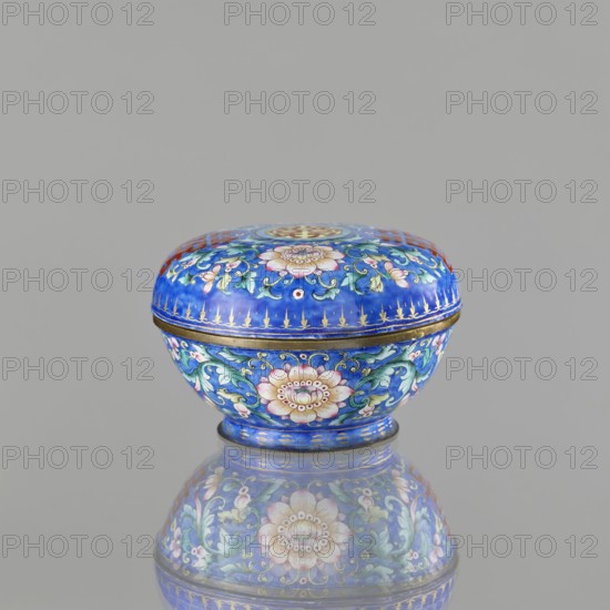Incense burner — bowl with a lid; maker, ; Chinese; Qing dynasty 1644–1911; 18th–19th century; painted enamel on metal; decoration on navy blue background with flower tendrils peony, bats, flowers, coins; character shuangxi double happiness — usually used in China in the context of marriage; ceremonial vessel / censer; export product; height 6.4 cm, diameter 9.7 cm, weight 0.17 kg., A small rounded decorative box with a domed lid sits centered on a reflective surface, the box predominantly featuring a bright cobalt blue background with floral and foliate patterns in pink, green, turquoise, white, and gold; the lid and body each display a large stylized blossom surrounded by curling green leaves and smaller pink flowers, with gold accents and a thin gold band where lid meets base, and the box’s reflection mirrors the same colors and motifs on the grayish surface beneath.