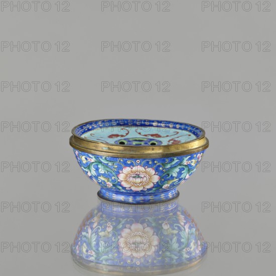Incense burner - bowl with a lid;, Chinese; Qing dynasty 1644–1911; 18th/19th century. Painted enamel decoration on a navy blue background featuring bats, flower tendrils peony, coins, and the character shuangxi double happiness, usually used in marriage contexts. Ceremonial vessel/censer for incense. Height 6.4 cm; diameter 9.7 cm; weight 0.17 kg., A small decorative bowl with a rounded shape and a metallic rim sits centered against a plain light gray background, its surface reflecting a mirrored image below; the bowl is predominantly cobalt blue with floral and foliate patterns in shades of pink, green, turquoise, white, and gold, featuring a prominent pinkish flower motif on the side surrounded by swirling green leaves and lighter blue accents, and the interior shows similar blue and turquoise tones with red curved elements and dark green circular shapes, while the metallic rim and base display a warm gold color.