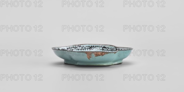 Plate, painted enamel on vessel, Chinese, Qing 1644–1911, 18th century, genre scenes, height 1.3 cm, width 7.5 cm, depth 9.1 cm., A shallow, irregularly shaped ceramic dish sits centered against a pale gray background; the dish is predominantly turquoise on its exterior with areas of exposed brownish material and fine hairline cracks, and its interior shows a lighter bluish-white glaze with a dark wavy decorative pattern near the rim; the rim itself appears darker with subtle wear, and the dish casts a soft shadow beneath it.