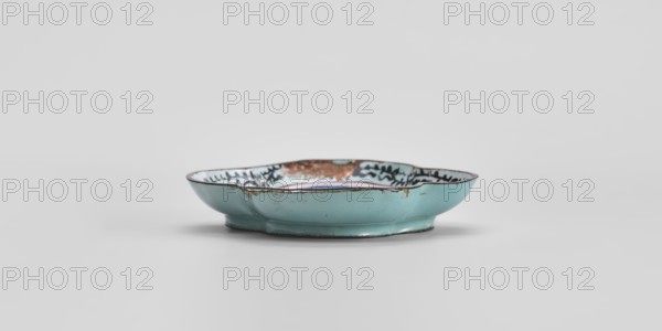 Plate, Chinese, painted enamel, Qing 1644–1911, 18th century, China; genre scenes; vessel; height 1.3 cm, width 7.5 cm, depth 9.1 cm., A shallow, scalloped-edged ceramic dish sits on a flat surface; the exterior and most of the interior visible are a pale turquoise color with areas of darker turquoise shading and a few spots of brownish discoloration along the rim and inner edge, and a band of mottled darker brown and black decoration is visible near the inner rim; the dish has a low foot and a slightly reflective glazed surface, with subtle shadows beneath it on a light gray background.