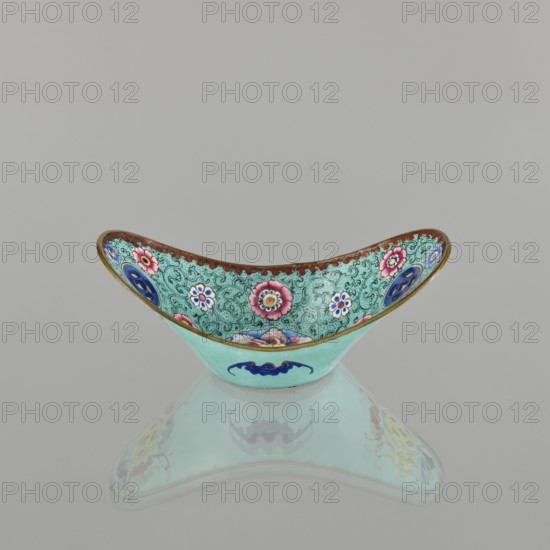 Bowl, painted enamel, Qing 1644–1911, Chinese, 18th/19th century. Ceramic vessel decorated with lotuses, coins, flower tendrils and bats iconography symbolizing happiness. Height 6.3 cm; width 8.5 cm; depth 15.3 cm., An ornamental bowl with a curved, crescent shape sits on a reflective surface, showing a mirrored underside; the bowl's exterior is a light turquoise with a dark blue stylized motif, while the interior features a detailed patterned background in turquoise with ornate swirls and a border in brownish-red, decorated with floral medallions in pink, white, blue, and yellow, and additional circular accents in deep blue and purple, all outlined with thin gold edging.