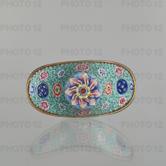 Bowl, painted enamel, Qing 1644–1911, China, 18th/19th century; decorated with boats, lotuses, coins, flower tendril, and bats iconography; symbolizing happiness; vessel; height 6.3 cm, width 8.5 cm, depth 15.3 cm., An oval decorative dish with a gold rim sits against a plain light gray background and casts a soft reflection below; the interior surface is covered in an intricate turquoise-green pattern with swirling lines and features a central circular floral motif in blue, pink, yellow, and red surrounded by several smaller flower designs in pink, blue, yellow, and white, as well as a few circular blue medallions.
