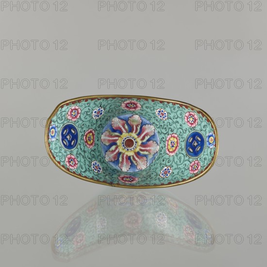 Bowl, painted enamel, Qing 1644–1911, China, 18th–19th century. Porcelain vessel decorated with boats, bats iconography, lotuses, coins, and floral tendrils—symbols of happiness. Height 6.3 cm; width 8.5 cm; depth 15.3 cm., An oval decorative bowl with a gold rim sits against a pale gray background, showing intricate enamel work in turquoise, blue, pink, red, yellow, white, and green; the interior features a central floral motif with radiating petal shapes in pink and white around a yellow and red center, surrounded by a densely patterned turquoise field with swirling green lines and several small pink and white flower motifs, plus a few circular blue medallions with cutout shapes; the bowl casts a soft reflection below it that mirrors the colors and patterns.