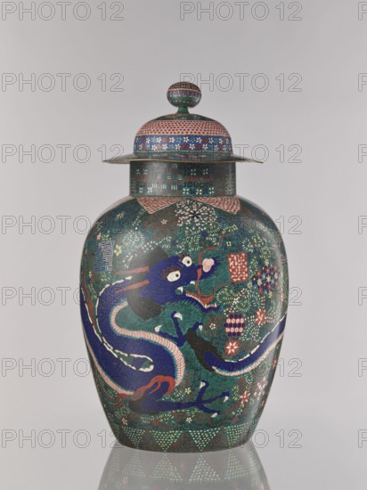 Vase with cover, Japanese, Edo 1603–1868 / Meiji 1868–1912, ca. 1860–1870, cloisonné enamel, Nagoya, Japan; vessel with cover, height 55.5 cm, diameter 35.0 cm. Decoration: covers; geometric-floral patterns including shippo, asanoha, kikko; dragons/Japanese dragon motif; floral ornament., A tall lidded vase sits against a pale background, covered in intricate decorative patterns and a large sinuous dragon motif. The vase features a domed lid with a round finial, a flared rim, and a rounded body that tapers slightly toward the base. The surface is densely decorated with floral and geometric designs rendered in deep green, dark blue, pink, red, teal, white, and black. A prominent dark blue dragon with pale pink accents and white eyes coils across the body, its claws and whiskers detailed in contrasting colors. Scattered floral clusters and repeated ornamental motifs in red, pink, white, and blue fill the background around the dragon. The lid and neck display bands of small repeating patt...