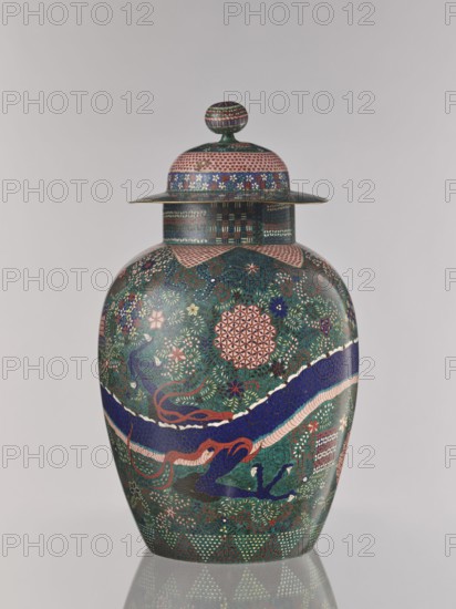 Vase with cover, Japanese, ca. 1860–1870 Edo/Meiji period, cloisonné enamel, Nagoya, Japan; vessel with cover, height 55.5 cm, diameter 35.0 cm; decorated with geometric-floral patterns, dragons Japanese dragon motif, floral ornament; patterns include shippo, asanoha, kikko., A lidded ceramic jar with a rounded body and a domed lid topped by a spherical finial, decorated all over with intricate repeating geometric and floral patterns in green, blue, pink, red, white, and gold tones; a broad diagonal band in deep blue with lighter and pink edging wraps around the body, intersecting detailed motifs of stylized flowers and foliage in green and pink, while the lid and neck show checkerboard and small floral bands in blue, pink, and gold; the jar sits on a reflective surface that shows a faint reflection beneath it.