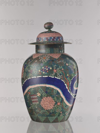 Vase with cover, ca. 1860–1870 late Edo–early Meiji, Japan, Nagoya. Cloisonné enamel vessel with cover, height 55.5 cm, diameter 35.0 cm. Decorated in cloisonné with geometric-floral patterns including shippo, asanoha, kikko, floral ornament, and dragons Japanese dragon motif., A lidded vase with a rounded body and a domed lid topped by a knob, decorated overall with dense small-scale patterns and floral motifs in a palette that includes green, blue, pink, red, white, and gold; a broad sinuous band of deep blue edged with pale pink winds around the body, set against a richly patterned green background filled with small flowers and leafy forms in red, white, blue, and gold; geometric medallions and patterned patches in pink and red appear amid the foliage; the lid and neck display bands of tiny repeating motifs and a band of small flowers in blue and white with pink borders; the knob atop the lid repeats the small-scale patterned ornamentation; the vase sits on a reflective surface that...