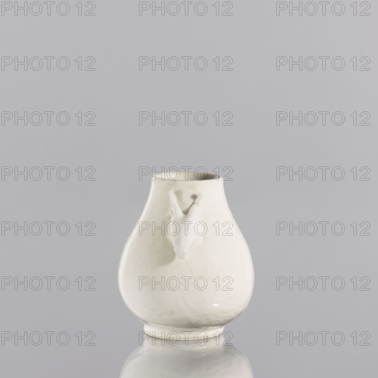 Vase, purchase provenance; Chinese; porcelain blanc de Chine decorative vessel; ceramics; Qing dynasty 1644–1911, 2nd quarter of the 17th century; China; vessel; height 6.7 cm, diameter 5.8 cm., A glossy white ceramic vessel with a rounded, bulbous body and a narrower neck, sitting on a reflective surface; the vessel has a small sculpted animal head protrusion on one side, smooth curved contours, subtle crackle-like surface patterns, and soft highlights and shadows; the visible colors are white, off-white, light gray, and pale reflections of the surrounding neutral background.