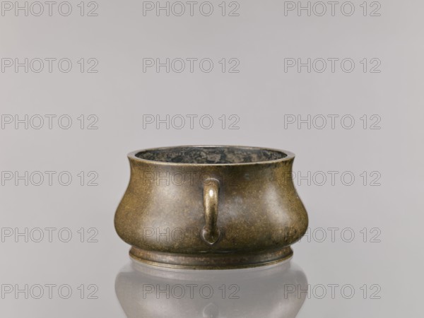 Censer, Chinese, Qing dynasty 1644–1911, 18th century; ceremonial/ritual vessel; backdated signatures; material not specified; height 8.5 cm, diameter 16.8 cm., A low, rounded metal vessel with a bulbous body and a slightly flared rim, showing a patinated surface in shades of brown, dark bronze, and muted green; a short curved handle projects from the front, and the interior appears darker with mottled gray and black tones; the vessel sits on a shallow circular base and casts a soft reflection on the pale gray surface beneath it, against a smooth light gray background.