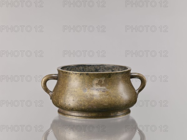 Censer, Chinese, Qing dynasty 1644–1911, 18th century. Bronze ritual/ceremonial vessel with backdated signatures. Height 8.5 cm; diameter 16.8 cm., A low, rounded metal vessel with a bulbous body and a short foot, shown from the front with a looped handle on each side; the vessel has a mottled, aged metallic surface in shades of bronze, brown, greenish patina, and darker mottling, and the interior appears darker with greenish and black tones; the piece sits on a reflective surface that creates a soft mirrored reflection beneath it, and the background is a smooth, light gray.