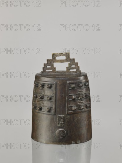 Bell linzhong, Chinese, Qing dynasty, Daoguang period 1821–1850, 1825. Bronze musical instrument idiophone/percussion, used in music and religious rites; decorated with ideograms and meander ornament. Dimensions: height 29.0 cm, width 20.0 cm, depth 17.0 cm., A bronze bell-like object with a stepped rectangular handle sits against a pale gray background; the handle has a patterned surface and the body of the object shows a dark brown and greenish patina with areas of lighter brown and black; the upper section features raised rectangular panels with a few rounded protrusions and recessed linear decorations, while the lower section is smoother with a circular raised emblem and subtle surface wear; the object rests on a reflective surface that mirrors its lower portion.