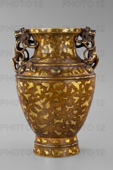 Vase on base. Chinese art, Chinese culture. Qing 1644–1911. Casts; vases; bases; antidated signatures; lion iconography. On a high foot. Decorated on the shoulders with six buttons with rosettes. Cast in bronze, inlaid with cold gold, dusting over lacquer. Varnished bronze, full-plastic relief and engraved decoration. Round base, bulging side decorated with openwork plant ornament, on four short legs one missing. 17th/18th century, China. Vessel, vase: height 26 cm, diameter 16.5 cm; base: height 5.3 cm, diameter 13.1 cm., provenance: gift., A large ornamental vase stands against a plain light gray background, showing a rounded body that narrows at the base and flares slightly at the rim. The surface of the vessel is predominantly brown with irregular patches of reflective gold scattered across it, creating a mottled pattern. Two ornate handles rise from the shoulders on opposite sides, each formed into a sculptural animal head and curling, sinuous limbs that attach to the neck, render...