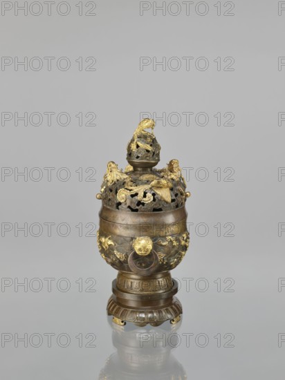Censer with a cover on a base., Qing style, Chinese, 18th century. Ceramic/metal vessel censer with high foot, openwork cover and handles; cover with removable knob. Decoration: dragons and hôô phoenix birds on the cover; various animals on the belly including tigers, birds, fish; dragon with a pearl, clouds, sea waves, geometric patterns, meander ornament. Ritual/ceremonial vessel. Height 22.0 cm, width 21.0 cm, depth 17.7 cm., The image shows an ornate metal vessel with a rounded body and a decorative lid, placed on a matching pedestal; the object features openwork and applied sculptural elements including stylized animal and floral forms, with visible areas of gold-colored gilding against a darker bronze or brown metal base; the lid is topped by a sculpted figure and the body displays relief ornament and ring handles, all reflected faintly on the glossy surface beneath, with a plain light gray background.