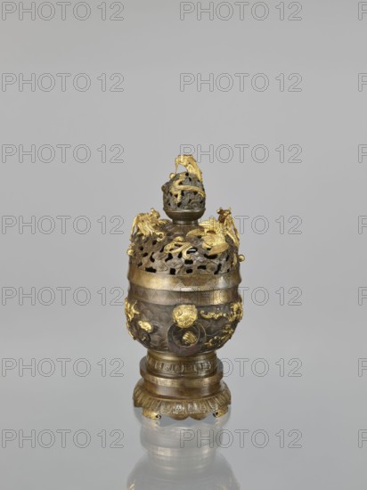 Censer with a cover on a base, maker, Qing style, Chinese art; Chinese culture. Subject and iconography: dragons including dragon with a pearl, hôô/phoenixes, tigers, birds, fish, sea waves, clouds, various animals; decorative motifs include meander and geometric patterns. Function: ceremonial/ritual vessel — censer with a high foot; openwork cover and handles; cover with removable knob. Materials/technique implied: vessel. Date: 18th century Qing, 1644–1911. Dimensions: height 22.0 cm, width 21.0 cm, depth 17.7 cm., An ornate metal vessel stands against a plain light gray background and rests on a reflective surface; the vessel is primarily bronze with gilded accents in gold, featuring an elaborate openwork lid topped by a spherical finial entwined with a sculpted creature, and the body is decorated with raised ornamental motifs including scrolling forms and sculpted animal-like figures; the base is tiered with carved fluting and petal-like elements, and the overall palette includes b...