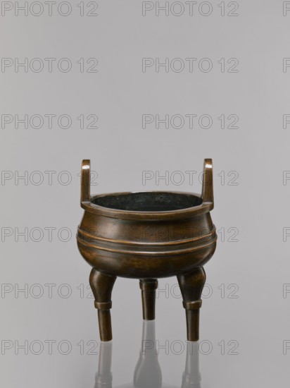 Ding type incense burner on a stand, Chinese, Qing dynasty 1644–1911, 19th century. Bronze ceremonial vessel incense burner with lotus motifs and stylized hieroglyphs FU happiness; iconography includes lotuses, bats symbolizing happiness, fo, tiger, and one hundred antiquities baigu ornament; meander ornament. Round wooden turned stand on five legs, on a pedestal in the shape of a lotus rosette. Incense burner: height 21 cm, diameter 15 cm. Base stand: height 7.5 cm, width 18.4 cm., A bronze tripod vessel with a rounded body and a dark interior sits against a neutral gray background, featuring two upright handles rising from the rim and three tapering legs that extend down to a reflective surface; the metal shows a brownish bronze patina with darker areas and subtle engraved patterns on the body, and the scene includes reflections of the legs on the glossy surface below.