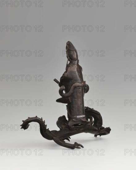 Guanyin on a dragon; creator, ; Chinese; Qing dynasty 1644–1911; Buddhism; bodhisattva/goddess of mercy; dragons iconography, dragon with a pearl; 18th century, China; sculpture, figurine; overall height 15 cm, width 7.1 cm; dragon: height 4 cm, width 8.3 cm., A dark brown sculptural object with a glossy surface stands on a pale background, featuring an upright central form that tapers toward the top and a looping element wrapped around it. The base extends into a sinuous, dragonlike appendage with ridged and spiky textures, clawed feet, and curved tail, all sharing the same dark brown tone. Subtle highlights of lighter brown and small areas of muted sheen appear where the surface catches light, and the surrounding space is a smooth gradient of pale gray to off-white.