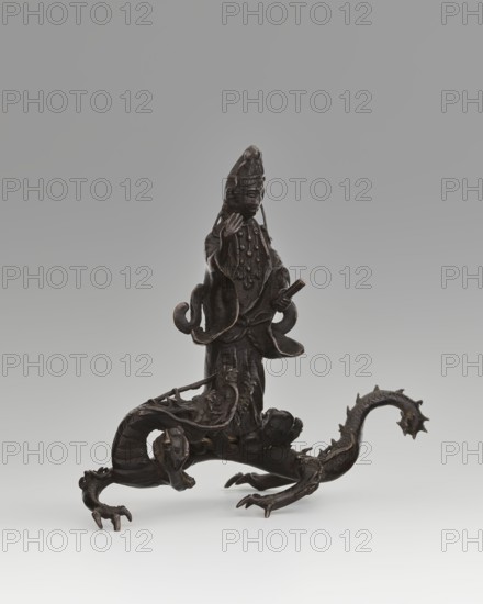 Guanyin on a dragon;, Chinese, Qing dynasty 1644–1911, 18th century; sculpture figurine depicting the bodhisattva Guanyin atop a dragon dragon with a pearl; material: Chinese art; subjects/iconography: Buddhism, bodhisattva, goddesses, mercy, dragons; dimensions: overall height 15 cm, width 7.1 cm; dragon: height 4 cm, width 8.3 cm., A dark brown metal sculpture depicting a robed figure standing on the back of a mythical creature with a long serpentine body and clawed limbs; the figure wears a tall headdress and layered robes with draped sleeves and rounded ornamental details, one hand raised near the face and the other holding a short cylindrical object; the creature beneath has a curled tail with spiny protrusions, a scaled body, and several clawed feet positioned on a neutral pale gray surface, set against a smooth gradient gray background.