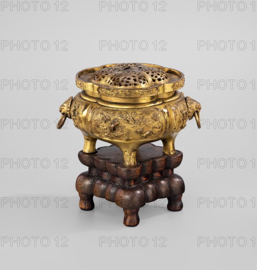 Incense burner with a cover on a base. Incense burner modeled on the ding type with a four-petal cross-section; openwork cover. Wooden, carved, quadrangular base on four legs. Chinese; Qing dynasty 1644–1911. Figural scenes. Vessel/censer. 18th century. Dimensions: censer height 6.7 cm, width 10.7 cm; base height 4.6 cm, width 6.9 cm., A small ornate vessel sits on a carved wooden stand; the vessel is metallic with a gold color and a slightly aged patina, featuring an openwork domed lid with decorative perforations and a round rim, a rounded body with embossed floral and bird motifs, short curved legs, and two small ring handles attached to sculpted animal head shapes on either side, all in gold tones. The stand beneath is wooden with a dark brown color and a polished surface, formed of layered, rounded cushion-like elements and short bulbous legs. The background is a neutral light gray.