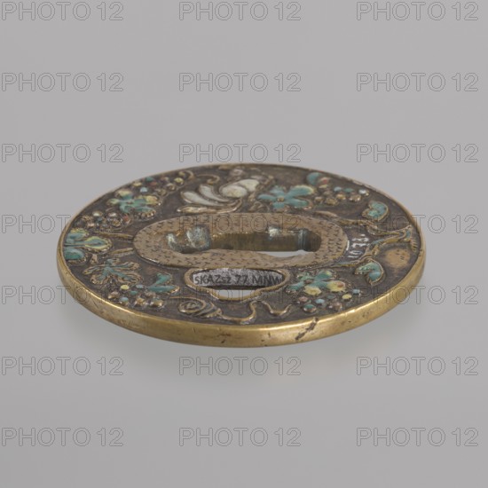 Crossguard tsuba, gift, Japanese, Edo period 1603–1868, 17th century. Round tsuba maru gata with slightly raised uchi kaeshi type edge and oval seppa dai. Dark patinated background highlighting the golden brass on the edge, around kôgai hitsuana and seppa dai. Relief decoration in colored enamels of a grape vine and a squirrel on both sides. Unsigned. Japan; tsuba; diameter 6.9 cm; thickness 0.5 cm., A round metal object with a raised oval opening in the center, decorated with floral and vine motifs in green, turquoise, yellow, brown, and gold tones; the metal shows areas of darker patina and bright brass edges, and the surface has textured, engraved patterns and small raised bead-like details.