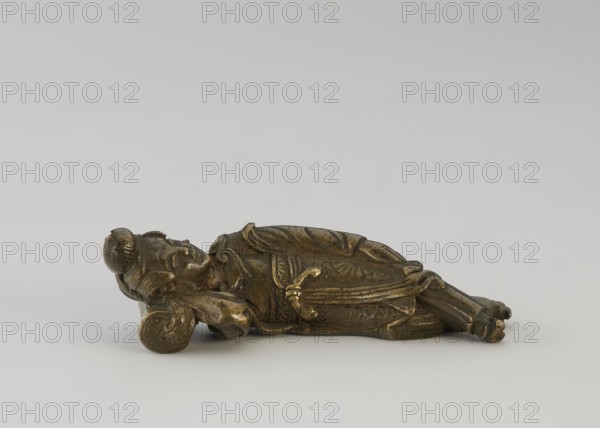Paperweight - lying woman;, ; Chinese; Chinese art; paperweight; Qing dynasty 1644–1911; 19th century; materials/implements for painting; subject: sleeping female figure on a pillow lady; figurine; height 2.5 cm, width 2.7 cm., A small reclining figurine made of a metallic material with a dark golden brown patina lies on its side on a light gray surface against a pale gray background; the figure has detailed carved or cast features including a rounded head with a bun, a relaxed facial expression, a hand supporting the head on a curved cushion-like element, draped clothing with carved folds and decorative patterns, and crossed legs with visible footwear, showing colors of dark gold, brown, and hints of darker greenish tarnish.