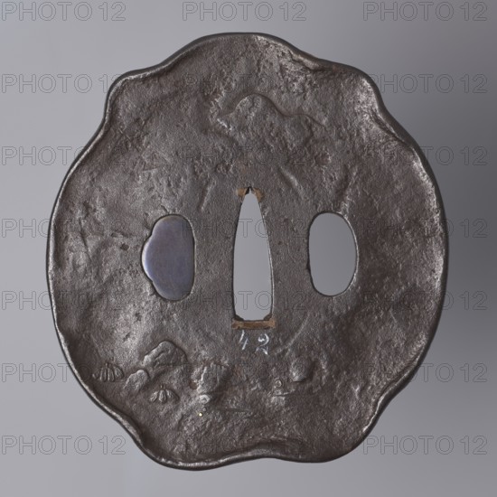 Crossguard tsuba, Kaneie role classification of creator, school craftsman author; Japanese; Edo period 1603–1868, 18th century; Japan, Yamashiro province, Fushimi city; tsuba in shape of a kobushi gata with slightly convex edge; kôgai hitsu closed with shakudô; decorated on both sides in low and high relief with details inlaid with gold and shakudô; obverse: Shôki demon slayer crouched under a tree; reverse: sketched landscape motif; materials: shakudô, gold; function: sword crossguard for katana; height 8.9 cm, width 9.6 cm, depth 0.65 cm., A dark brown irregular round metal object with a scalloped edge, showing a textured, slightly pitted surface and a subtle sheen; it has a central vertical elongated opening and two oval openings flanking it, one of which contains a smooth bluish-in-gray inset; the surface shows a few raised, rounded bumps and shallow depressions suggesting a rough relief, with small areas of lighter brown where the metal appears worn; the background is a smooth lig...