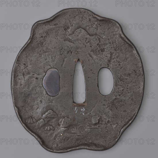 Crossguard tsuba, Kaneie role classification of creator, school craftsman author; Japanese; Edo period 1603–1868, 18th century; Yamashiro, Fushimi, Japan. Tsuba in the shape of a kobushi gata with a slightly convex edge; kôgai hitsu closed with shakudô. Decorated on both sides in low and high relief with details inlaid with gold and shakudô. Obverse: Shôki the demon slayer crouched under a tree; reverse: sketched landscape motif. Materials: shakudô and gold. Function: sword crossguard for katana. Dimensions: height 8.9 cm; width 9.6 cm; depth 0.65 cm., A roughly circular, irregularly edged dark metal object with a textured, pitted surface; the metal appears mainly dark gray to black with areas of lighter gray highlights and a bluish oval inset on one side. The piece has three central openings: a tall, narrow tapered one in the middle and two oval openings flanking it, revealing a smooth gray background through them. There are a few small raised and indented marks and rough patches acro...