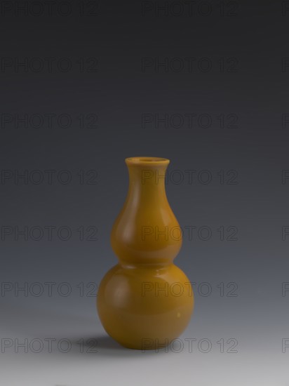 Vase, Chinese art, Chinese culture, Qing 1644–1911, Qing style, double gourds, stained glass, gourds, vases, yellow glass, cast and cut, opaque, 18th century, China, vessel, height 16.5 cm, diameter 8 cm, weight 0.40 kg, A smooth glossy gourd-shaped ceramic vase in a warm mustard yellow stands centered against a gradient dark-to-light gray background, showing subtle reflections and highlights on its curved surfaces and a soft shadow beneath it.