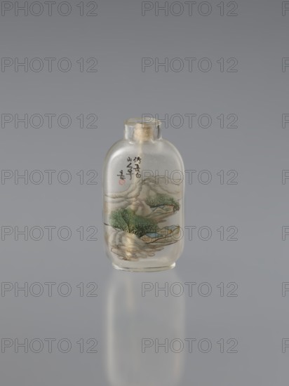 Snuffbox with spoon, provenance noted, Chinese, Chinese art; vials; landscapes, mountain landscapes; Qing dynasty 1644–1911; rounded sides; colorful decoration painted with natural paints; ink on the inside: landscape of the Changbai Mountains, inscription, seal; bone spoon glued to a green stone head; 19th century; China; vessel; height 6.4 cm, width 3.5 cm., A small clear glass bottle with a rounded rectangular shape and a short neck sealed with a pale cork sits centered against a smooth gray background; the bottle shows a painted scene inside featuring green trees, pale blue roofs, tan and beige landforms, and shaded grayish mountains, along with a few brushstroke markings in dark ink and a small red circular mark.