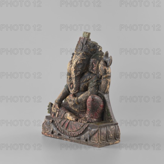 Ganesha, late 18th century, Nepal; sculpture of Ganesha with lotus iconography, elephants, axe, mounts, flowers, rats; associated with Shaivism and Hinduism; materials/technique implied Indian art; bracelets, necklaces; height 26.0 cm, width 19.5 cm, depth 8.2 cm., A carved figure of an elephant-headed deity seated on a decorated base, with a worn surface showing layers of paint in colors including dark brown, black, red, green, and traces of yellow and beige; the figure has an ornate headdress, a curved trunk, rounded limbs, and textured details on the clothing and base, and a few areas of chipped or flaked paint revealing underlying material.